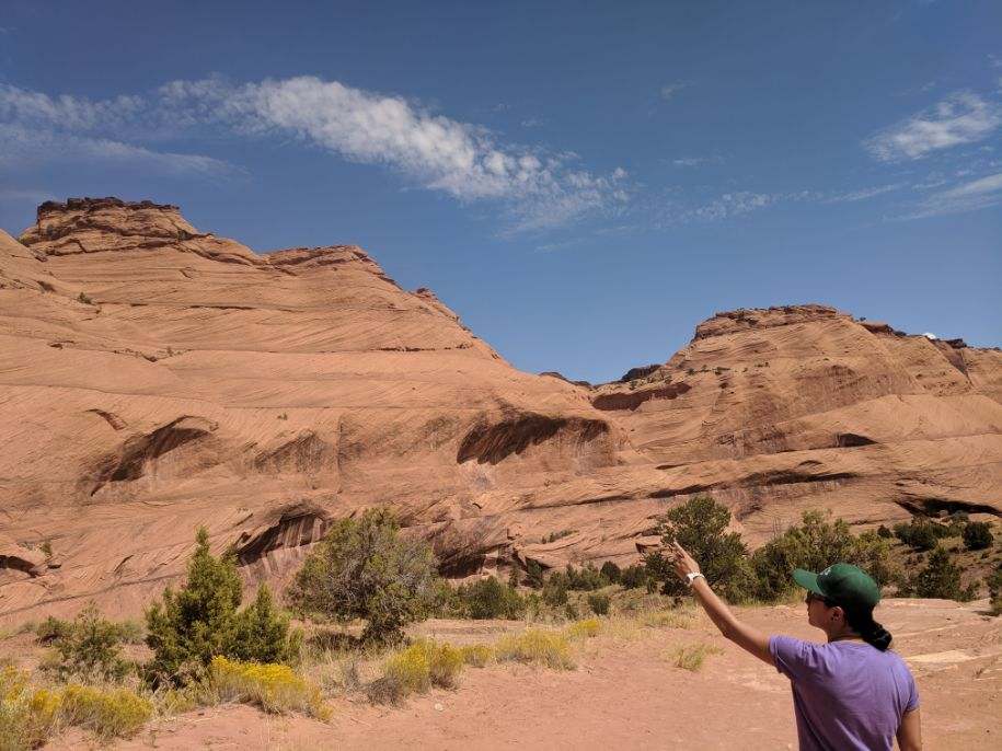 Landscape photo of southwestern desert mountains, with a person in the lower right foreground pointing in the distance